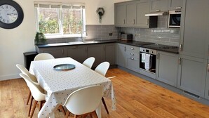 A modern kitchen with grey cabinets, a built-in oven, and a dining area with a table and chairs.