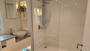 Un baño moderno con ducha de vidrio, lavamanos blanco y piso de mármol.