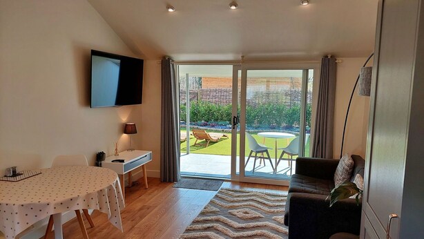 Una sala moderna con comedor, sofá, televisión y puerta corrediza de vidrio que da a un jardín.