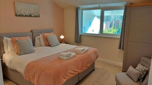 Un dormitorio con cama, almohadas, una lámpara de noche, una ventana y vistas al exterior.