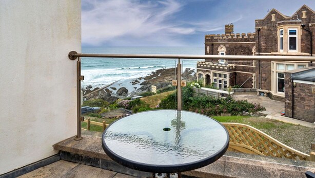 Varanda com mesa de vidro e vista para a costa rochosa e edifícios históricos.