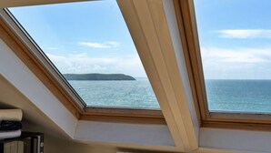 Quarto com claraboias e vista para o mar e uma ilha ao longe.