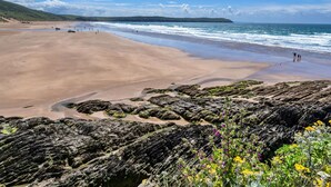 Uma praia com terreno rochoso em primeiro plano e uma área de areia.