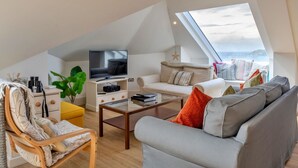 Uma sala de estar moderna estilo loft, com uma televisão grande, assentos confortáveis, uma mesa de centro e vista para o mar.