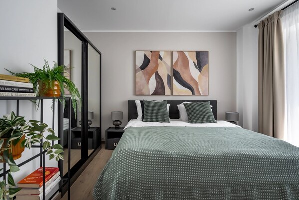 Une chambre moderne avec un grand lit, une table de chevet, une bibliothèque et des œuvres d’art abstraites accrochées au mur.