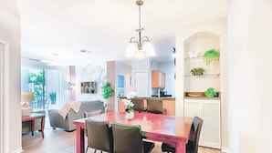 A dining area with a wooden table and chairs, a chandelier, and a view of the kitchen and living area. - 8908 Family Fun in Kissimmee Spacious 4-bedroom Apartment Near Theme Parks (Kissimmee)