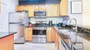 A compact kitchen with stainless steel appliances, wooden cabinets, and a granite countertop. - 8908 Family Fun in Kissimmee Spacious 4-bedroom Apartment Near Theme Parks (Kissimmee)