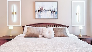 A neatly made bed with a patterned bedspread, flanked by two bedside tables with lamps, and a large abstract painting on the wall above. - 8908 Family Fun in Kissimmee Spacious 4-bedroom Apartment Near Theme Parks (Kissimmee)