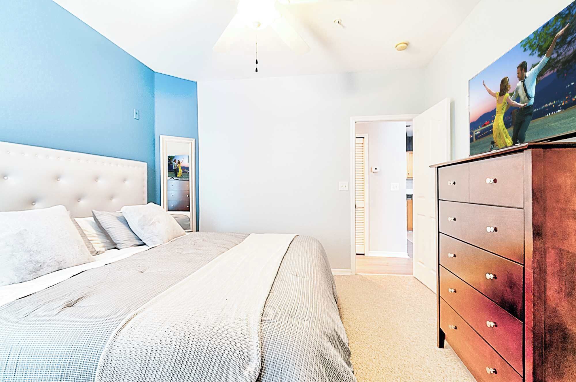 A bedroom with a tufted headboard, a large bed, a wooden dresser, and a framed picture on the wall.