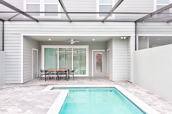 Un patio couvert avec une piscine, une table et des chaises, ainsi qu’un ventilateur de plafond.