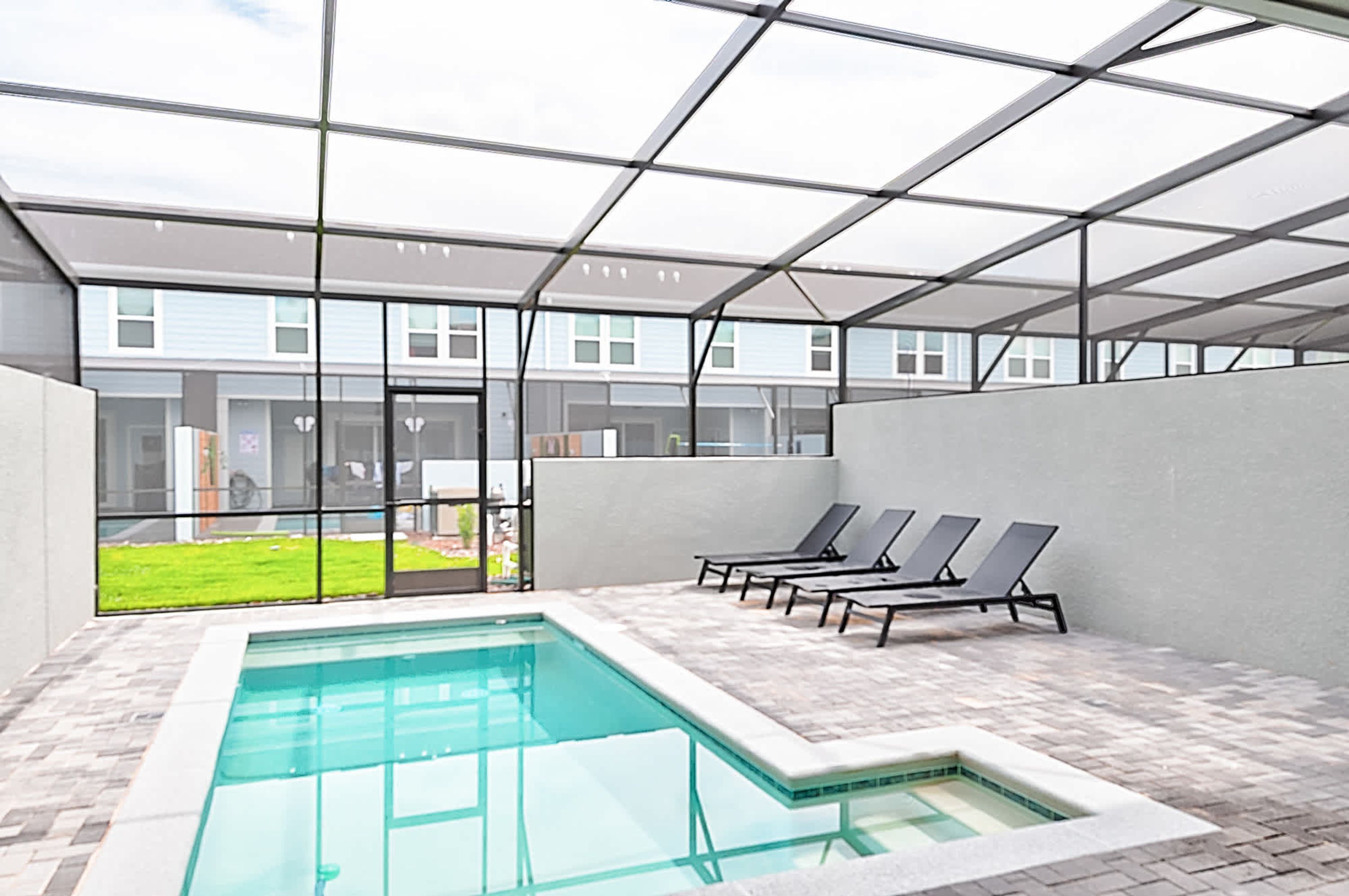 A pool area with a glass enclosure, lounge chairs, and a view of a building with windows.