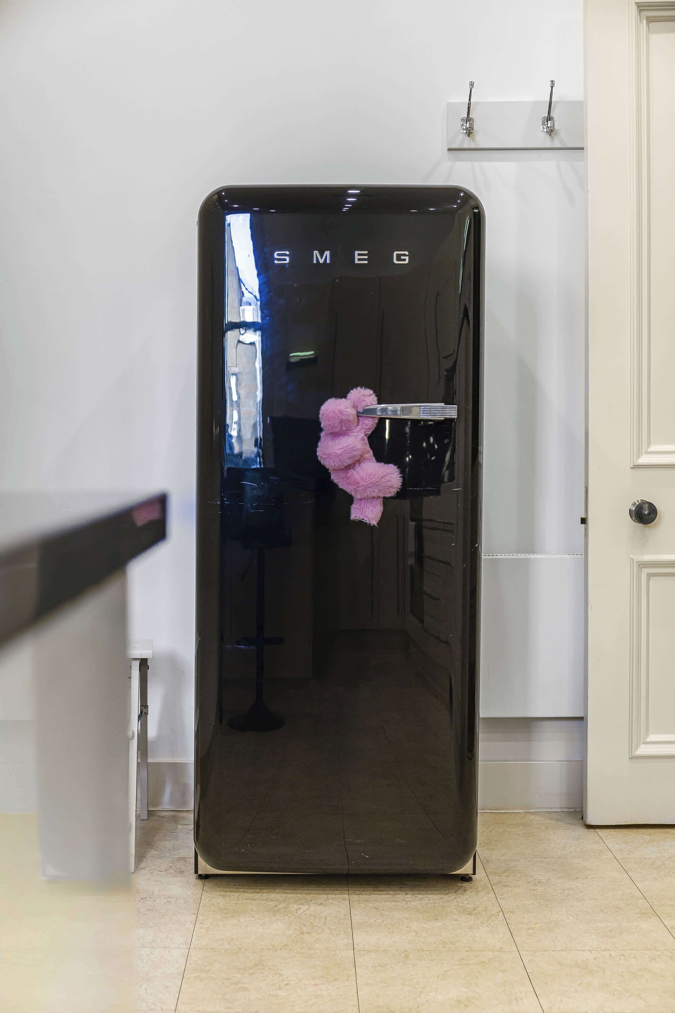 A black refrigerator with the brand name "SMEG" on it, placed in a kitchen with white cabinets and a white door in the background.