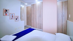 A bedroom with a bed, a blue bedspread, wooden wardrobes, and framed pictures on the wall.