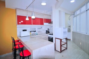 A modern kitchen with a central island, red and white cabinets, and a bar area with red chairs. - Conforto e Estilo em Copacabana D056 (Rio de Janeiro)