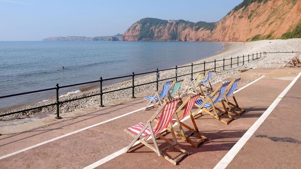 A beach with a row of beach chairs and a fence along the water's edge.