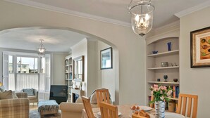 A spacious living room with a dining area, featuring a fireplace, a large window, and a bookshelf.