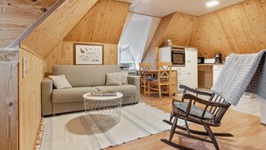 A cozy loft-style room with a sofa, a rocking chair, a dining table, and a kitchen area. - Apartment 'Peace and Nature' with Private Garden and Wi-Fi (Demmin)
