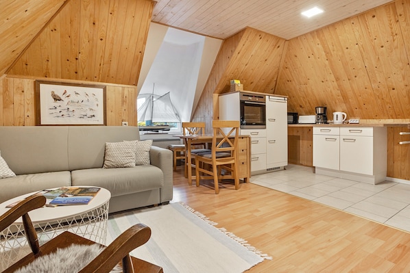 A cozy loft-style room with a wooden ceiling, a kitchenette, a dining area, and a sofa.