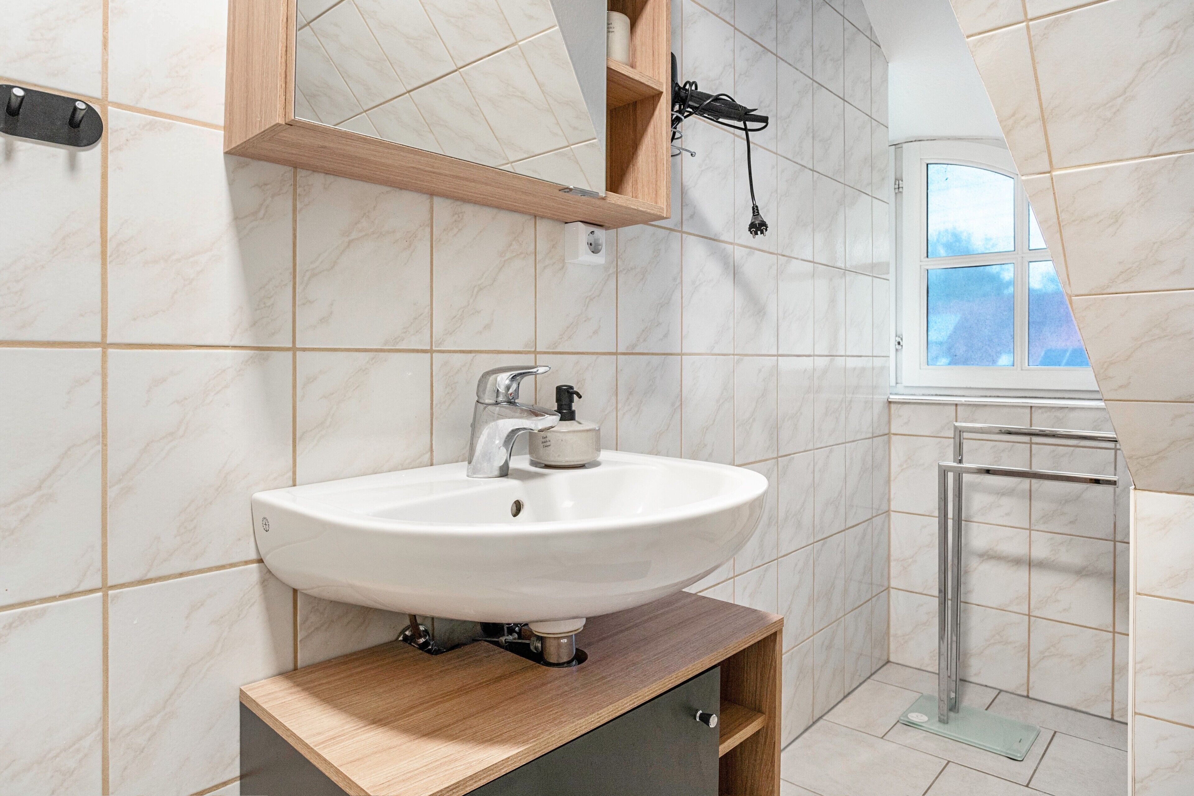 Une salle de bain avec un lavabo blanc, un meuble en bois et une fenêtre donnant sur un beau paysage.