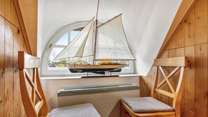 A room with a sloped ceiling, a sailboat model, two wooden chairs, and a window with a view of houses. - Apartment 'Peace and Nature' with Private Garden and Wi-Fi (Demmin)