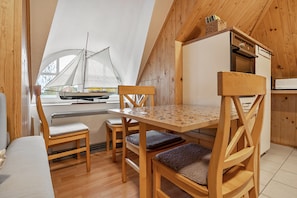 A wooden interior with a dining table, chairs, a small boat model, and a kitchen area.