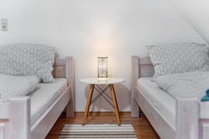 A small, cozy room with two single beds, a round table with a lamp, and a wooden floor.