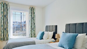 Een hotelkamer met twee bedden, een raam met zonwering en uitzicht op gebouwen.