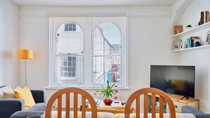 Een woonkamer met een eettafel gedekt voor twee personen, een bank, een televisie en een boekenkast.