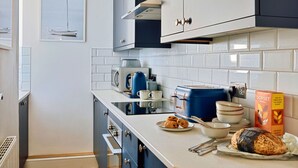 Een keuken met witte kastjes, een broodrooster, een waterkoker en een brood op het aanrecht.