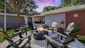 An outdoor patio with Adirondack chairs, a fire pit, string lights, and a 'DO NOT ENTER' sign.