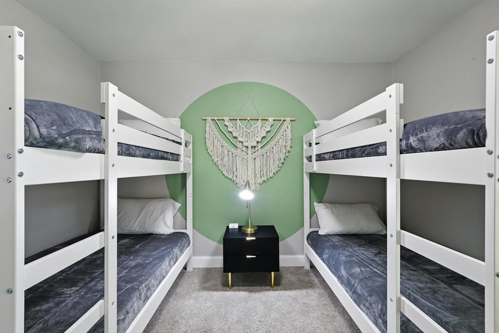 A bunk bed room with a green accent wall, a decorative macrame piece, and a bedside lamp.