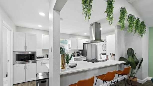 A modern kitchen with white cabinets, stainless steel appliances, and a central island with bar stools.