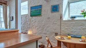 A cozy kitchen with a wooden counter, a round dining table, and a chair. There is a window with a view of the outside, a lamp on the table, and a painting on the wall. - Beautiful  villa for 4 people with WIFI and pets allowed (Cawsand)