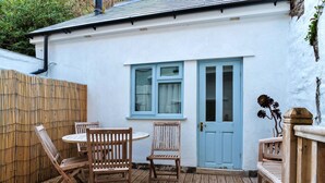 A wooden deck with a round table and four chairs, a blue door, and a window with curtains. - Wonderful  villa for 6 people with WIFI, terrace and pets allowed (Cawsand)