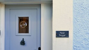 A light blue door with a small window and a brass door knocker. A black metal door handle is visible, and a sign reading "Nor Nour" is mounted on the wall to the right of the door. - Wonderful  villa for 6 people with WIFI, terrace and pets allowed (Cawsand)