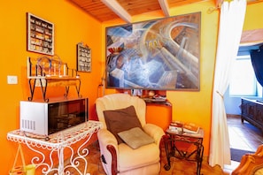 A room with a large abstract painting, a white armchair with a brown cushion, a small table with a book, and a white cabinet with shelves. - Bed and Breakfast 'Breizh' with Private Terrace, Shared Garden and Wi-Fi (CAST)