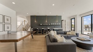 Un salon moderne avec une table basse en bois, un canapé gris et un coin repas agrémenté d’un mur en briques et de luminaires suspendus.