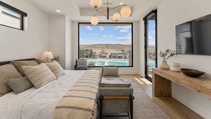 Une chambre moderne avec un grand lit, un banc en bois, une télévision et une vue sur la ville et l’eau.