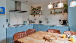 A modern kitchen with blue cabinets, a wooden dining table, and hanging pendant lights. - Beautiful  villa for 8 people with WIFI and pets allowed (Cawsand)
