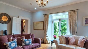 A living room with two sofas, a chandelier, a clock, and a window with curtains. - Beautiful  villa for 8 people with WIFI and pets allowed (Cawsand)