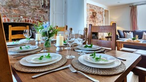 A dining table set for six with plates, glasses, and candles, in a room with a brick wall and a fireplace.