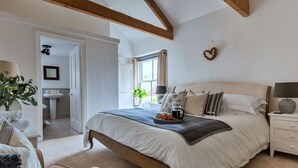 A bedroom with a large bed, bedside tables, a nightstand, a chair, and a view of the bathroom.