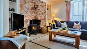 A cozy living room with a brick fireplace, a television on a wooden stand, a sofa, a coffee table, and a bookshelf.