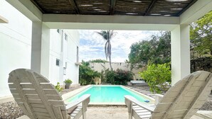 A pool area with two lounge chairs facing the pool, surrounded by a white building and greenery. - Apartment for 8 Guests in Sabanilla a Few Steps from the Sea (Sabanilla)