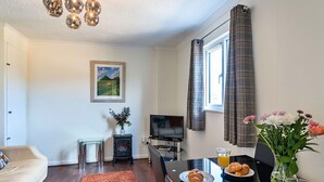 A modern living room with a sofa, a coffee table, a fireplace, and a dining area with breakfast items. - Beautiful  villa for 4 people with WIFI and TV (Glastonbury)