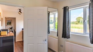 A bedroom with a bed, a window with curtains, a radiator, and a door leading to another room. - Beautiful  villa for 4 people with WIFI and TV (Glastonbury)