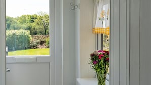 Une pièce avec une fenêtre, une porte et un banc près de la fenêtre agrémenté d’un vase de fleurs.