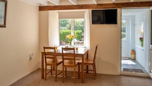 Un coin repas avec une table et des chaises en bois, un luminaire au plafond et une vue sur l’extérieur par une fenêtre.