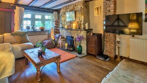 A cozy living room with exposed wooden beams, a stone fireplace, a television, and a comfortable seating area. - Stunning  villa for 4 people with WIFI and pets allowed (Felbridge)
