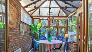 A conservatory with a brick wall, a table with chairs, a vase with flowers, and a hanging light fixture. - Stunning  villa for 4 people with WIFI and pets allowed (Felbridge)